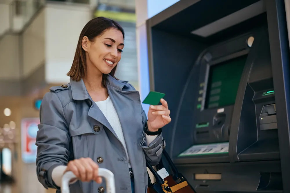 Happy traveler using her credit card at ATM at the airport. 