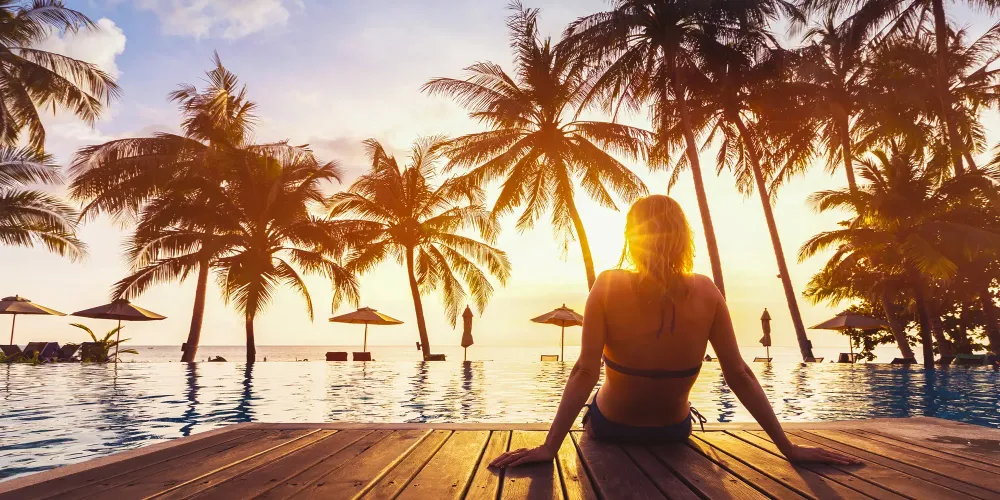 Woman enjoying vacation holidays at luxurious beachfront hotel resort with swimming pool and tropical lansdcape near the beach