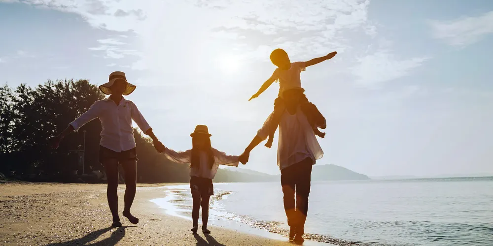 Holiday travel concept, Summer vacations. Happy family are having fun on a tropical beach in sunset. Father and mother and children playing together outdoor on sea.; Courtesy Sumala Chidchoi/Shutterstock