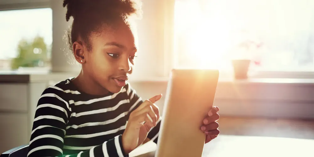 Young African-American Girl Surfing the Internet Using Tablet computer at the Table Inside Home.; Courtesy of Flamingo Images/Shutterstock
