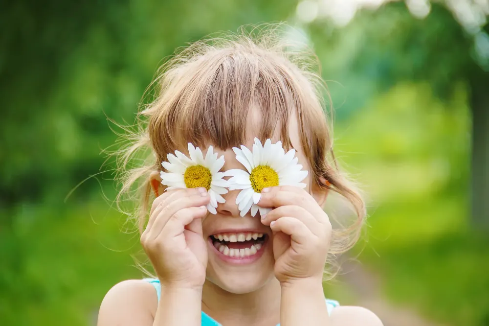 Child holding chamomile flowers in front of her eyes