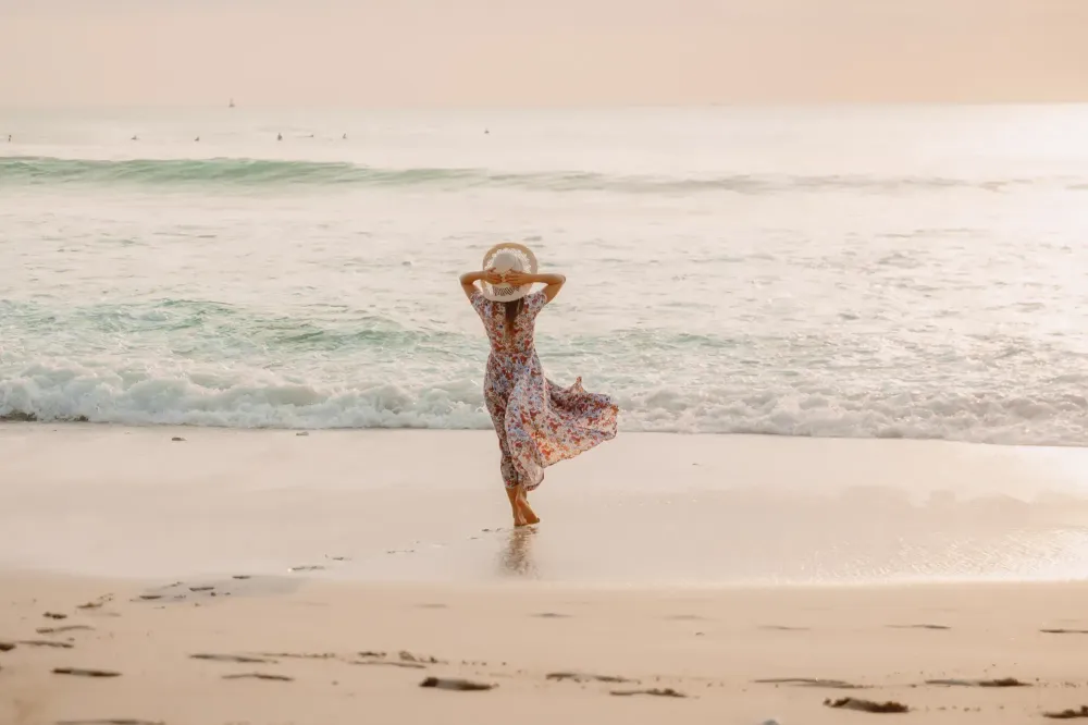 Woman standing by ocean in a dress and sunhat