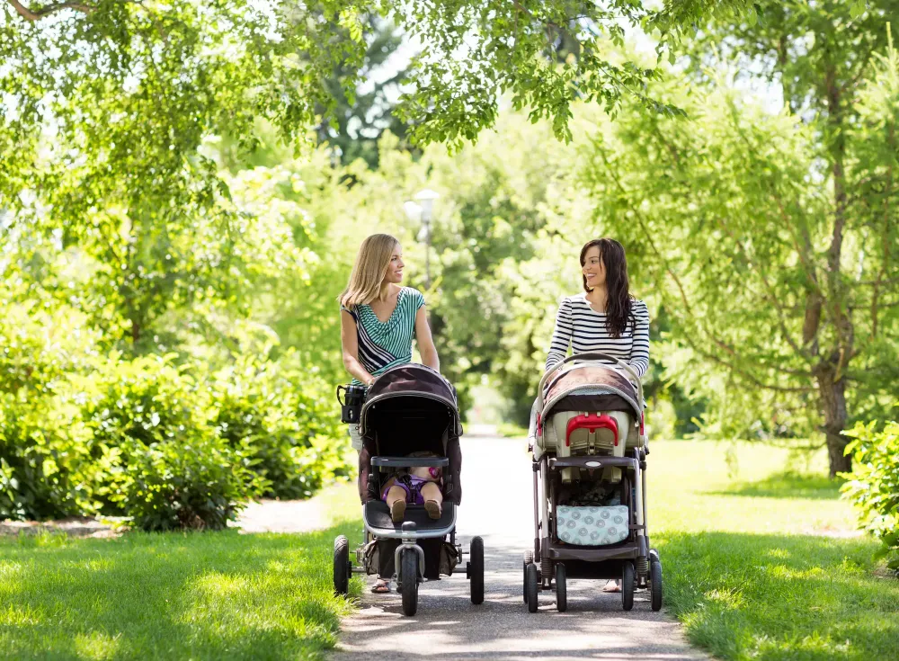 Two women pushing two babies in two strollers in the park