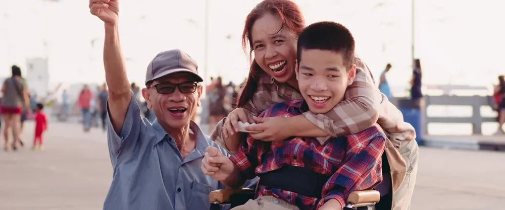 Two parents and a child in a wheelchair on the boardwalk by a beach
