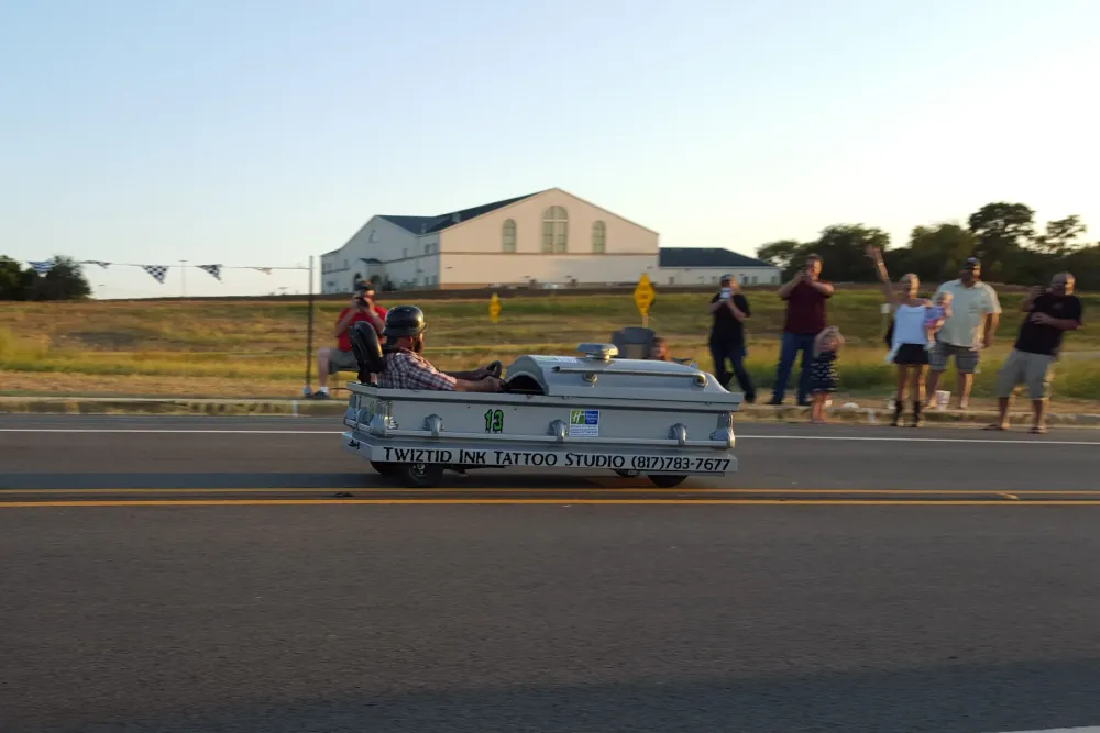 Man riding in a Soapbox Derby car made out of a coffin. 