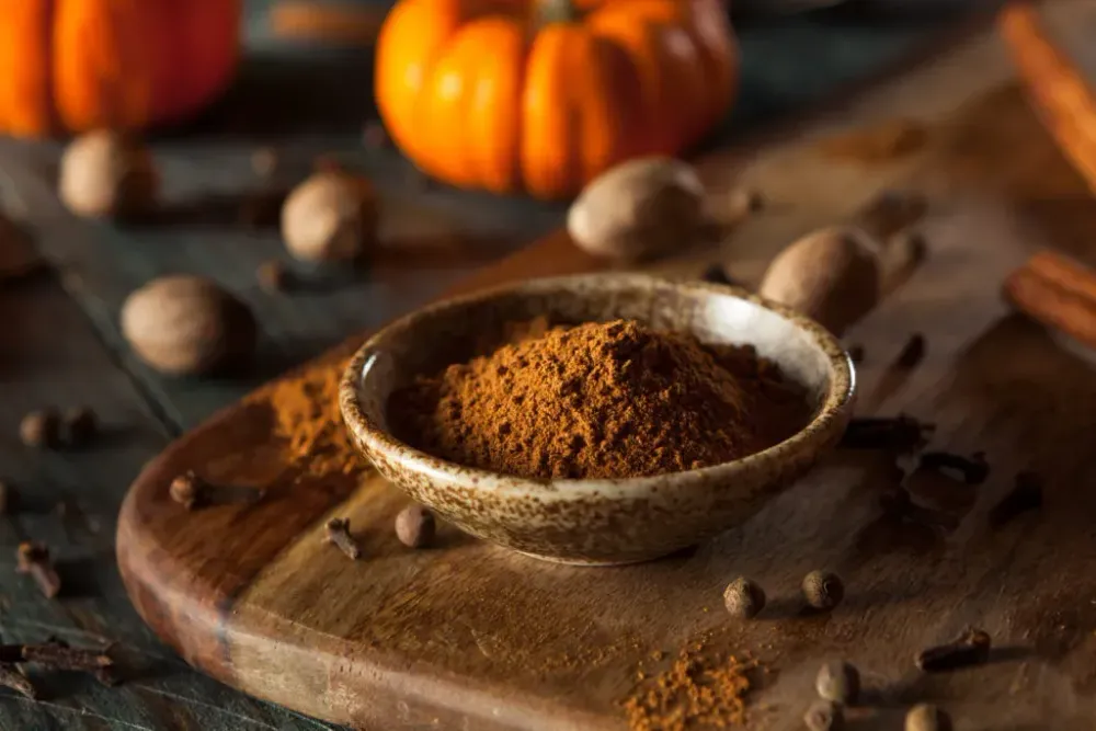 A small, ceramic bowl of pumpkin spice mixture surrounded by small pumpkins and nuts