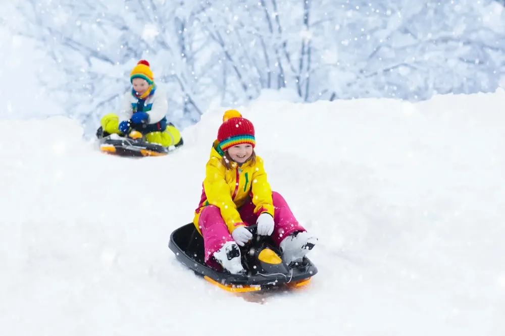 Two children in winter gear sledding down a hill