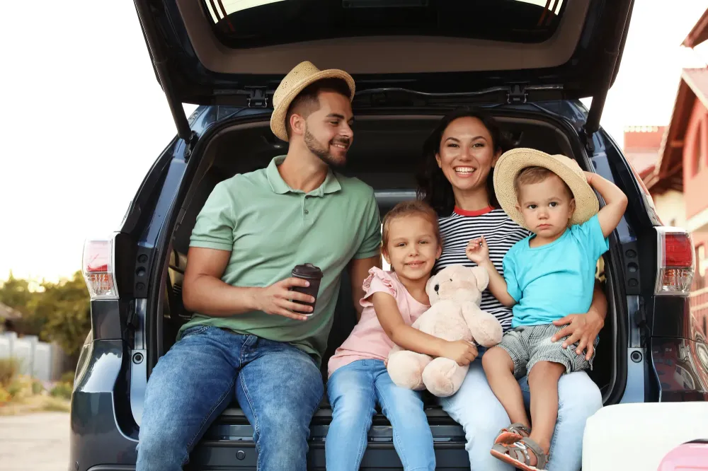 Family of four sitting in the trunk of their car with suitcases nearby