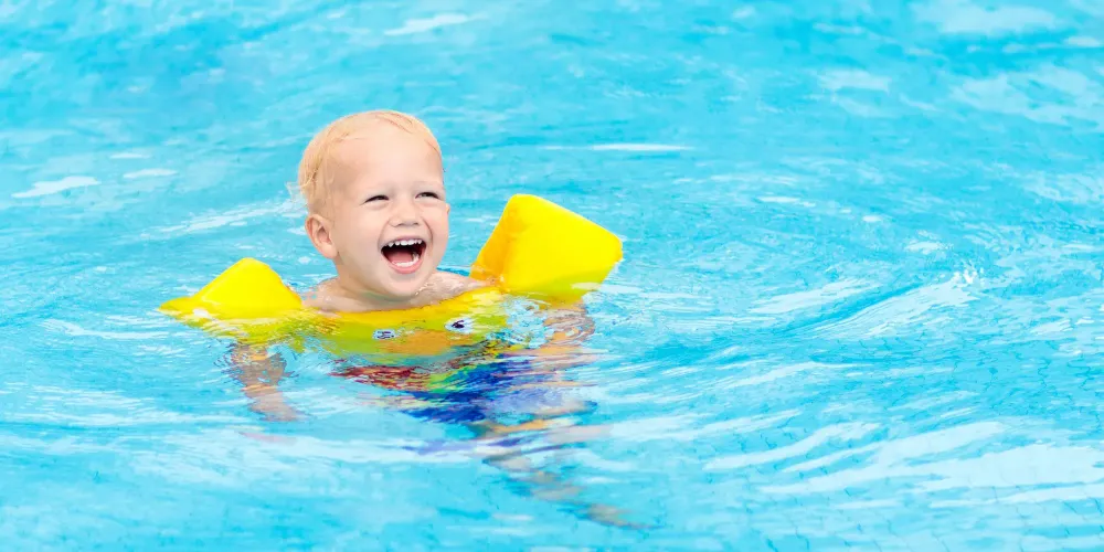 Toddler swimming in pool with swim floaties on; Courtesy of FamVeld/Shutterstock.com