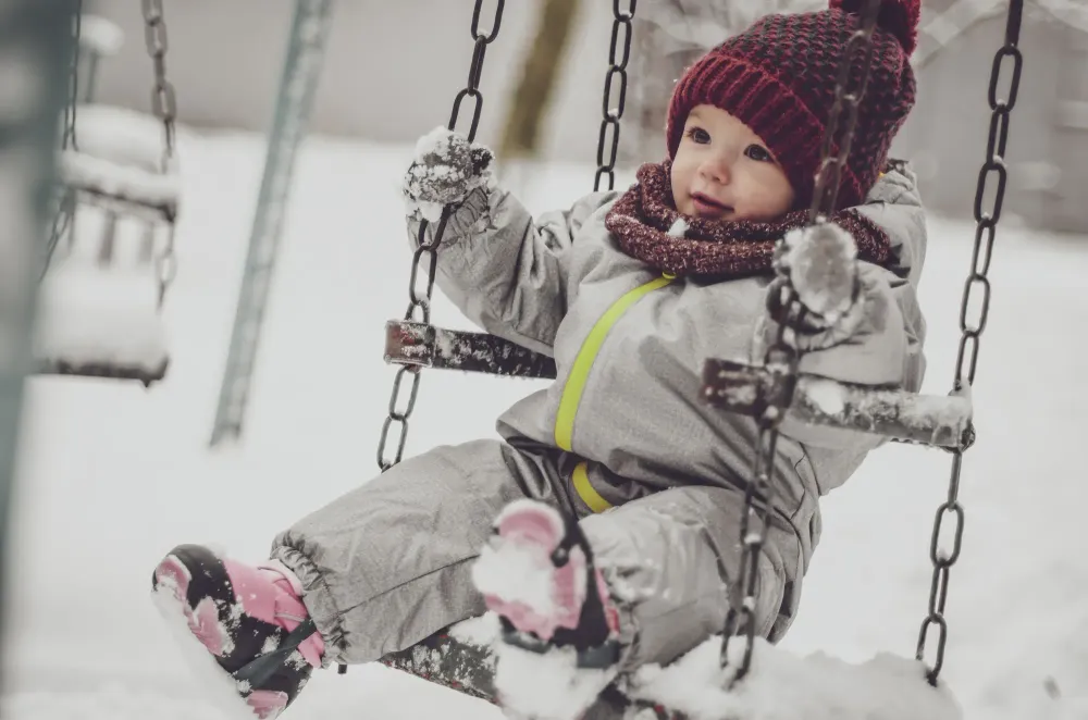 Toddler bundled in snow gear on a swing