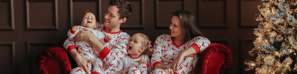 Family wearing matching holiday pajamas on a couch next to a Christmas tree