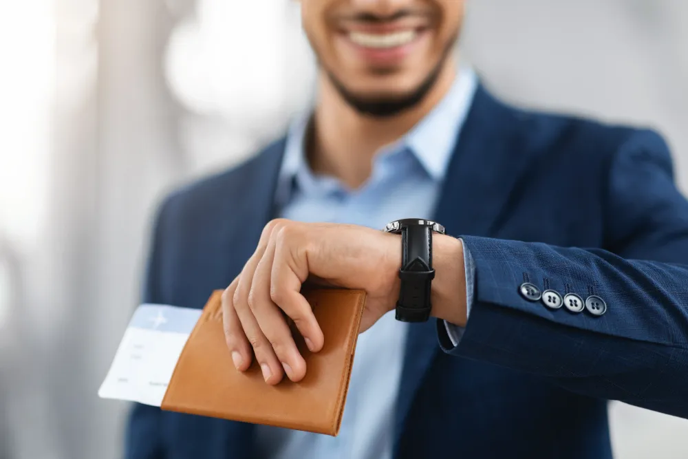 Smiling Man Holding Passport With Tickets And Looking At Wristwatch