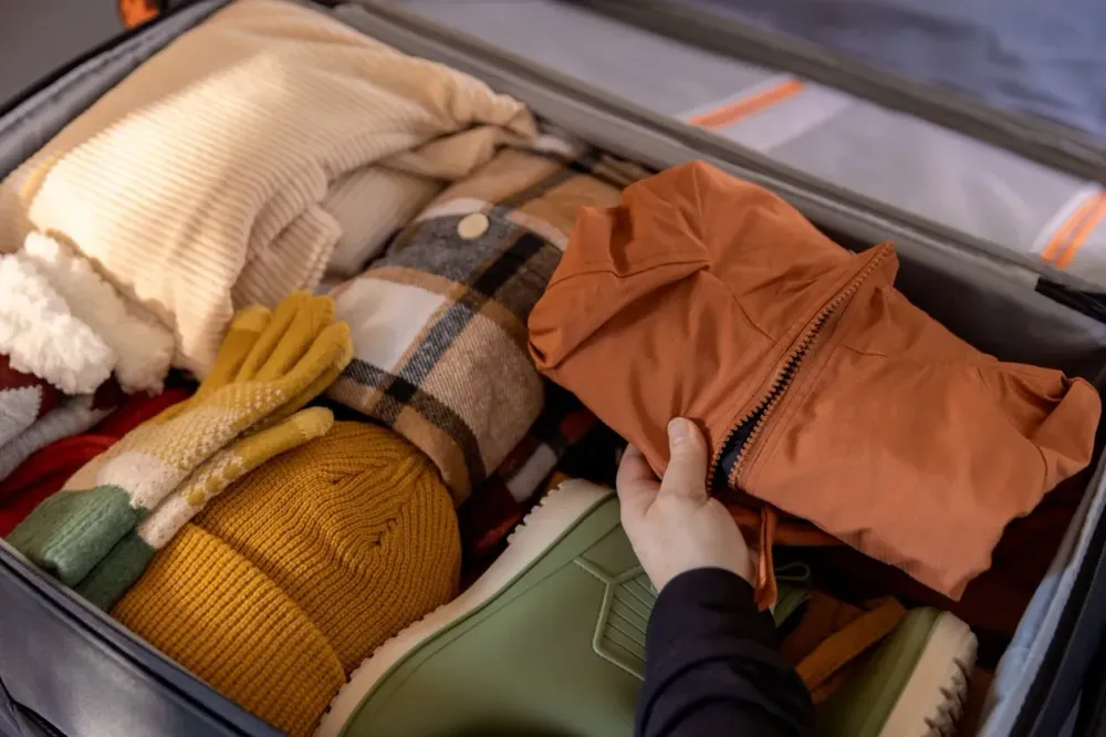 A woman's hand packing winter clothes and accessories in suitcase